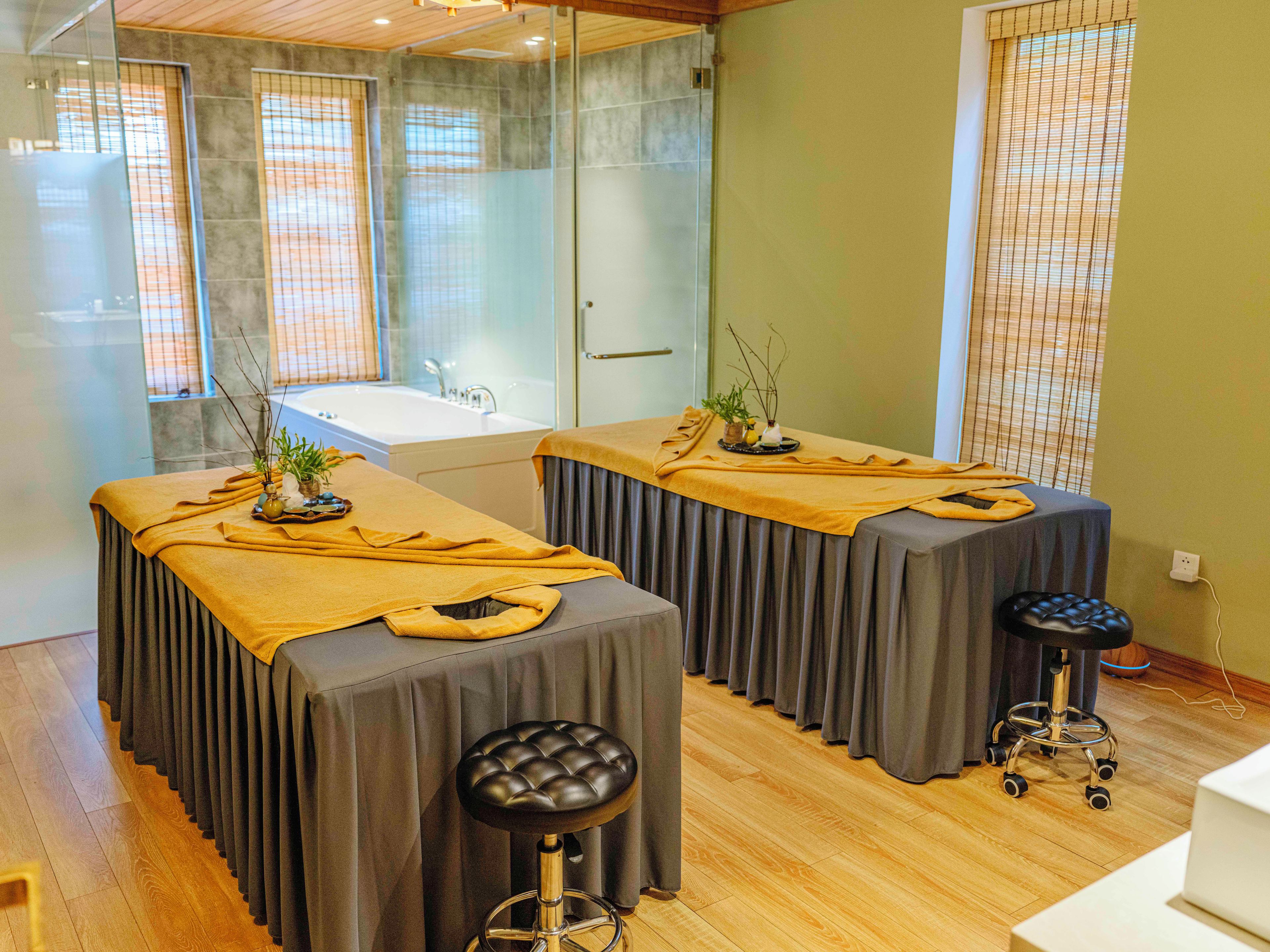 A spa room with two massage tables, a bathtub, and a wooden floor.