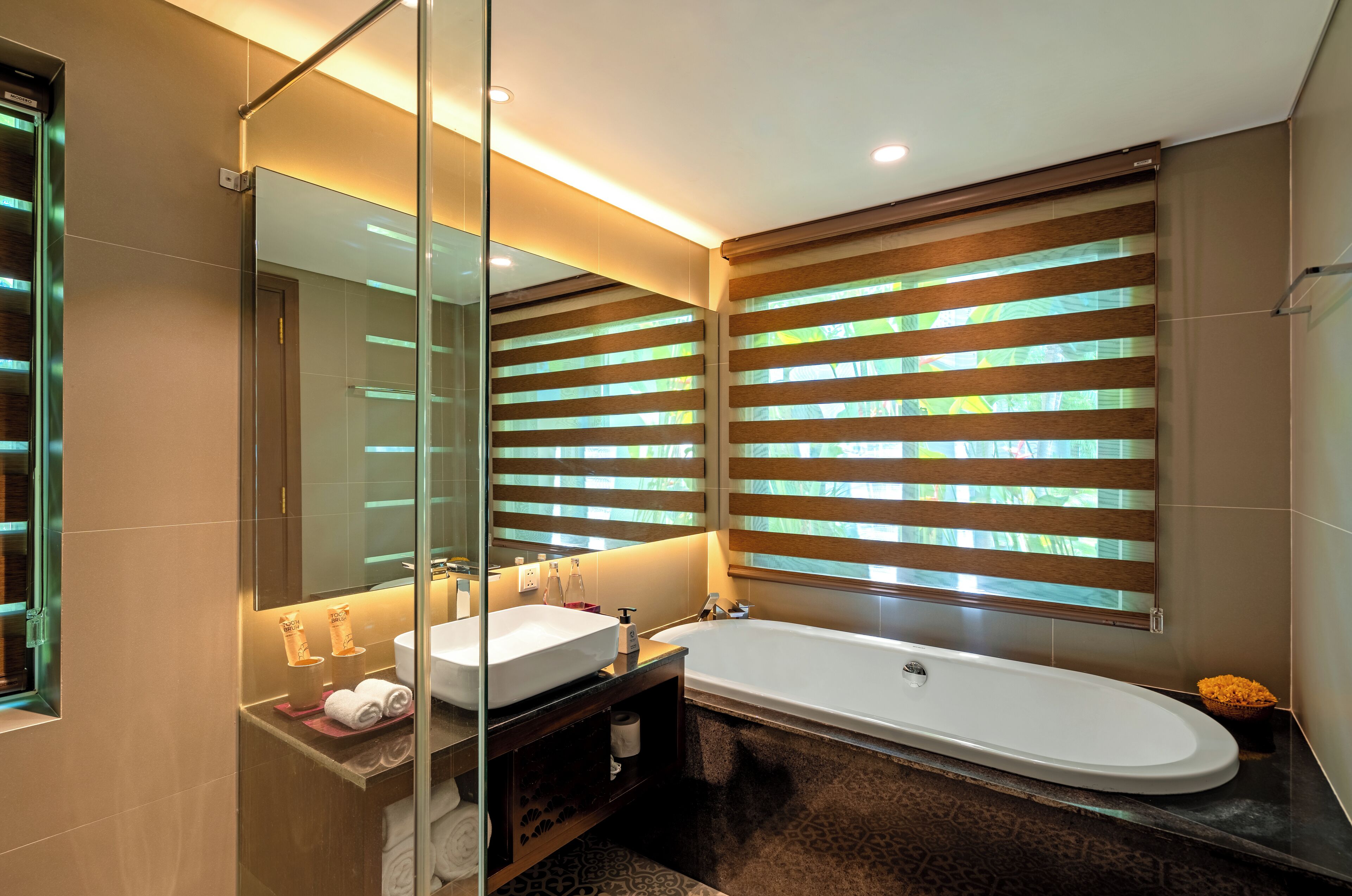 A modern bathroom with a large mirror, a white bathtub, and a vanity with a sink and towel rack.