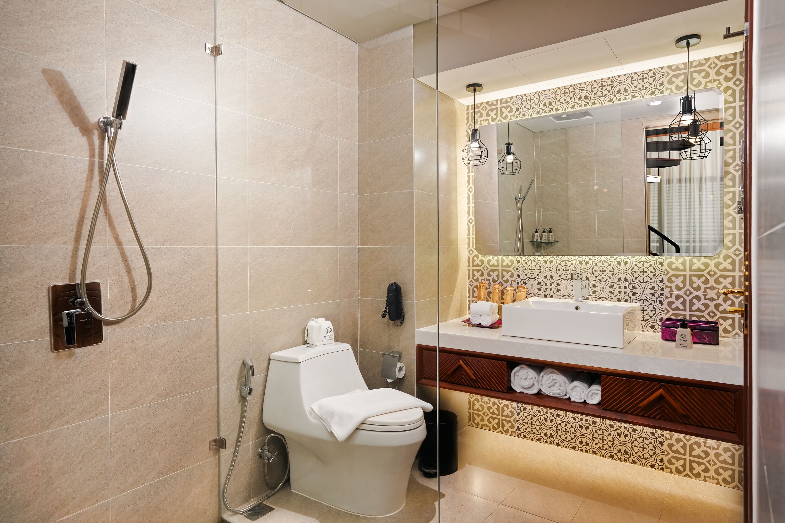 A modern bathroom with a glass-enclosed shower, a white toilet, a vanity with a mirror, and a patterned wall.