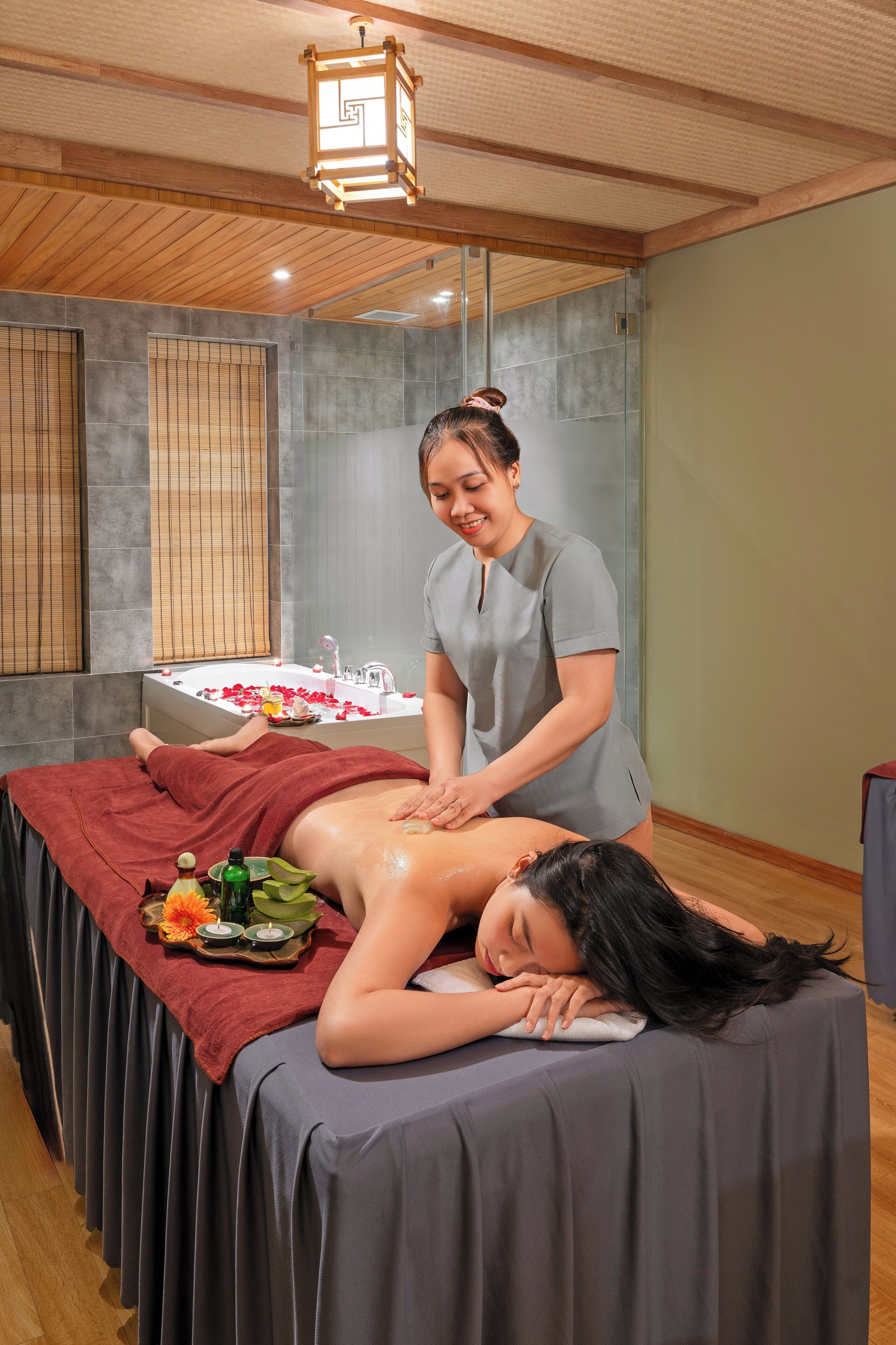 A massage therapy room with a wooden ceiling, a massage table, and a small table with candles and a tray of rose petals.