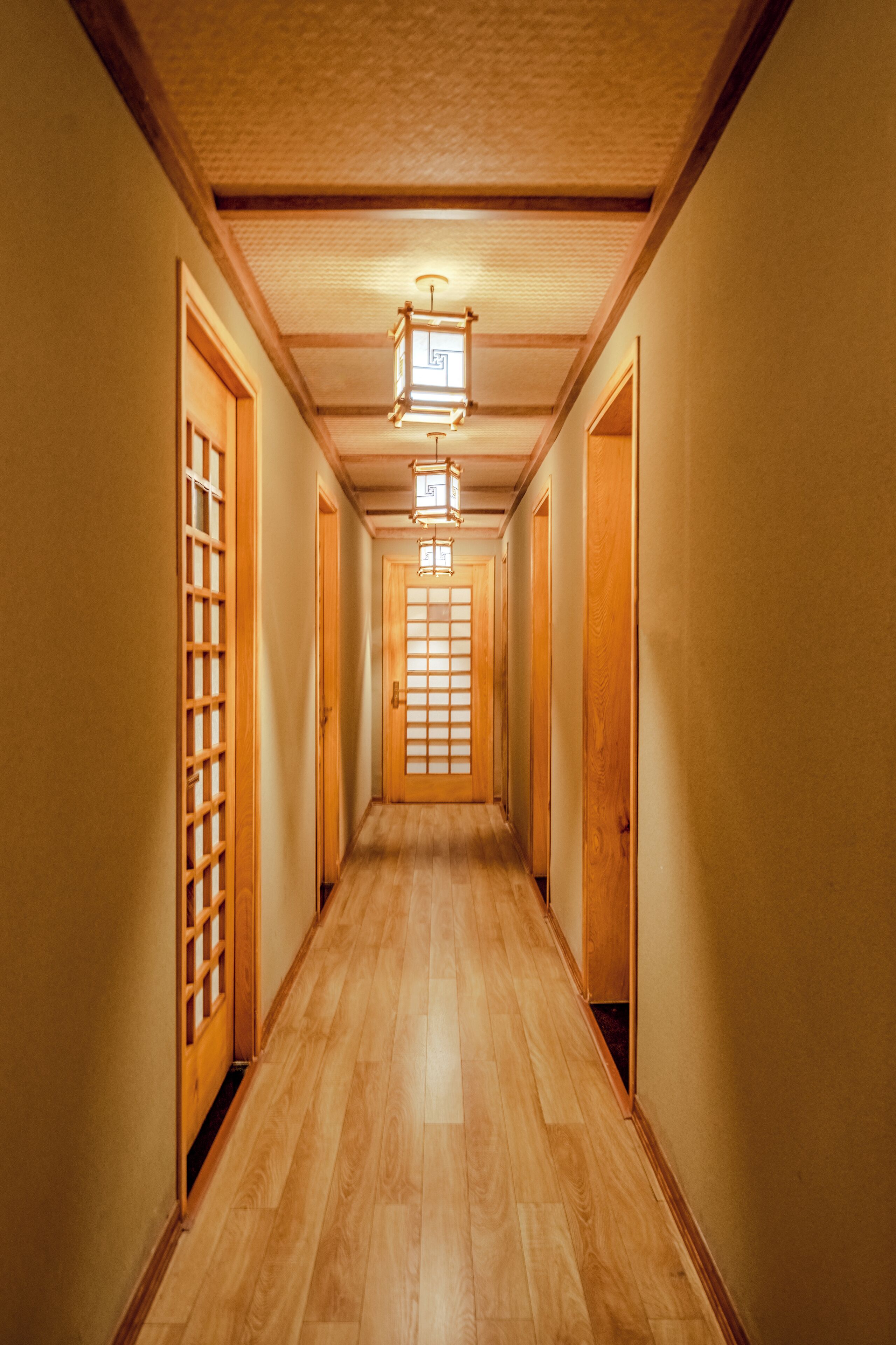 Un long couloir étroit, avec des portes en bois et un plancher en bois.