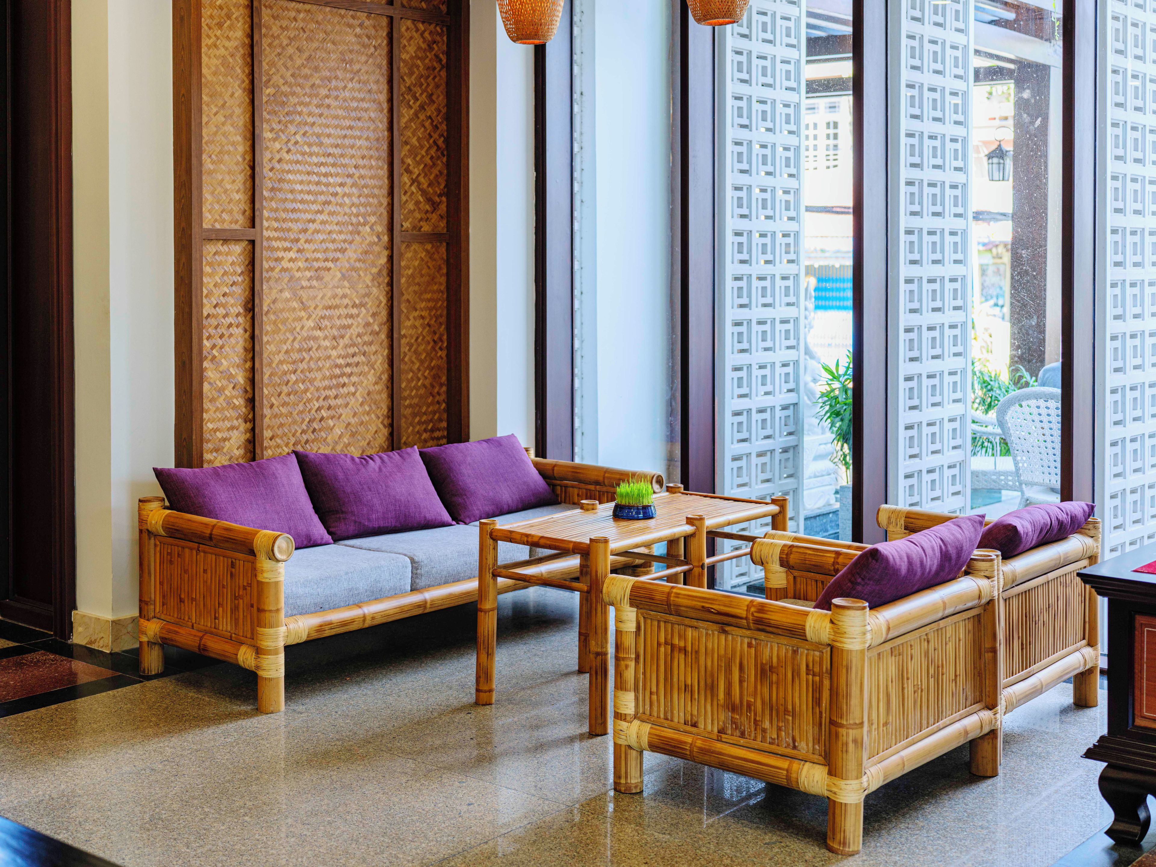 A room with a bamboo sofa, a small table, and a view through large windows.