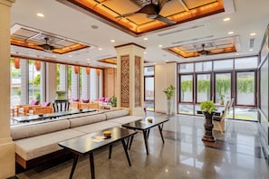 A spacious lobby with a seating area, a reception desk, and large windows offering views of the outdoors. - The Saga Hotel Hoi An (Da Nang)