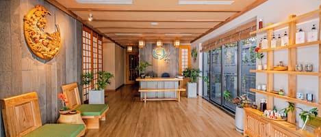 A wooden reception desk with a sign, wooden benches with green cushions, and a wall with a large decorative piece.