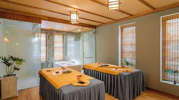 A spa room with two massage tables, a glass shower enclosure, and wooden flooring.