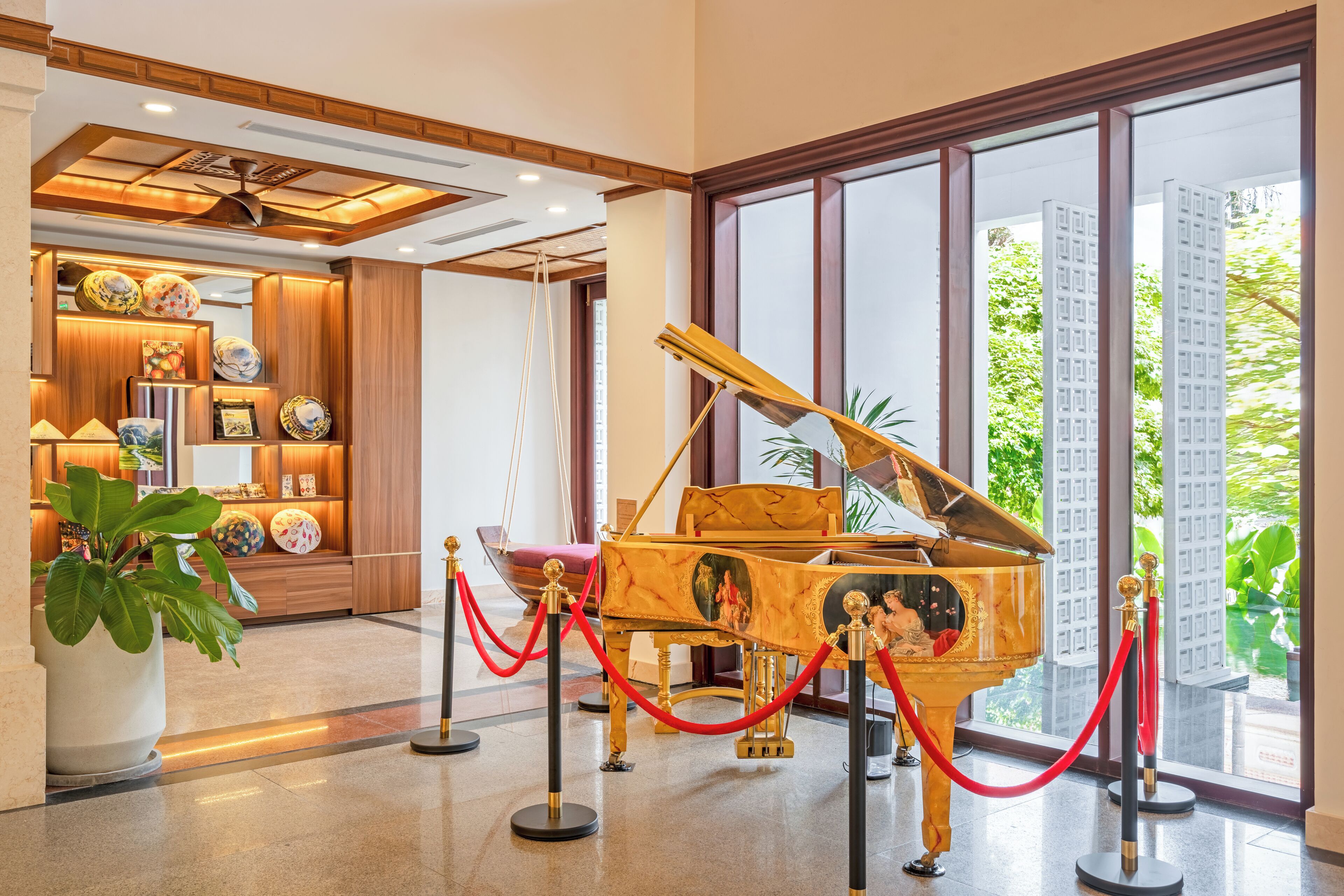Un gran piano en un vestíbulo bien iluminado, con un amplio ventanal, una planta en maceta y una exhibición de platos decorativos.