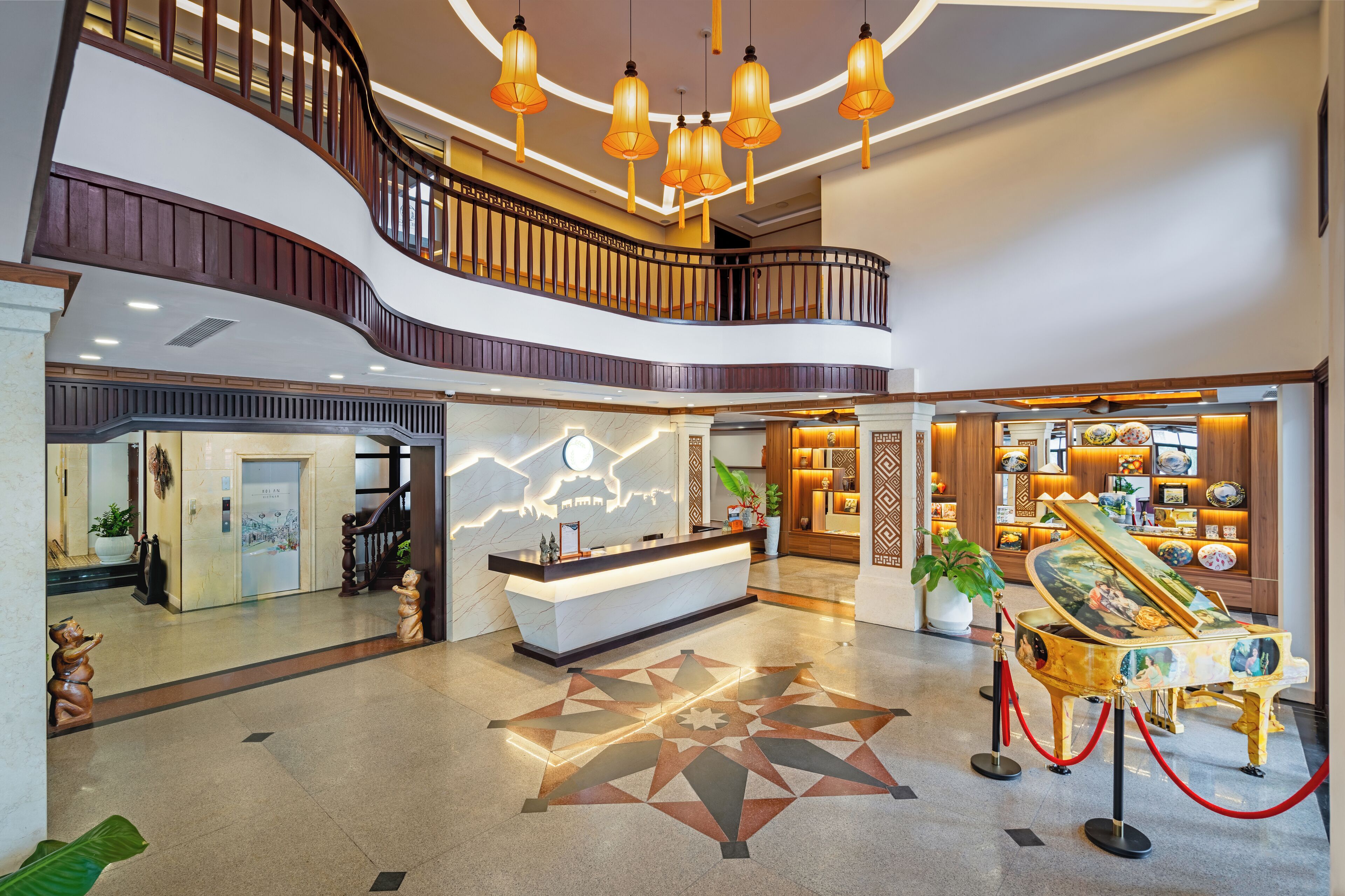 A hotel lobby with a reception desk, a piano, a staircase, and a decorative floor pattern.