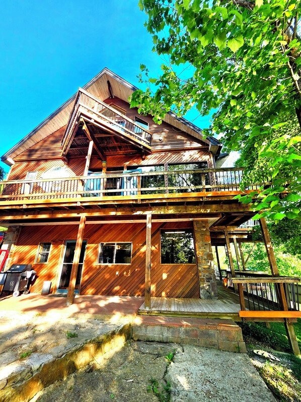 A wooden cabin with a balcony, a wooden deck, and a stone pathway leading to the entrance.