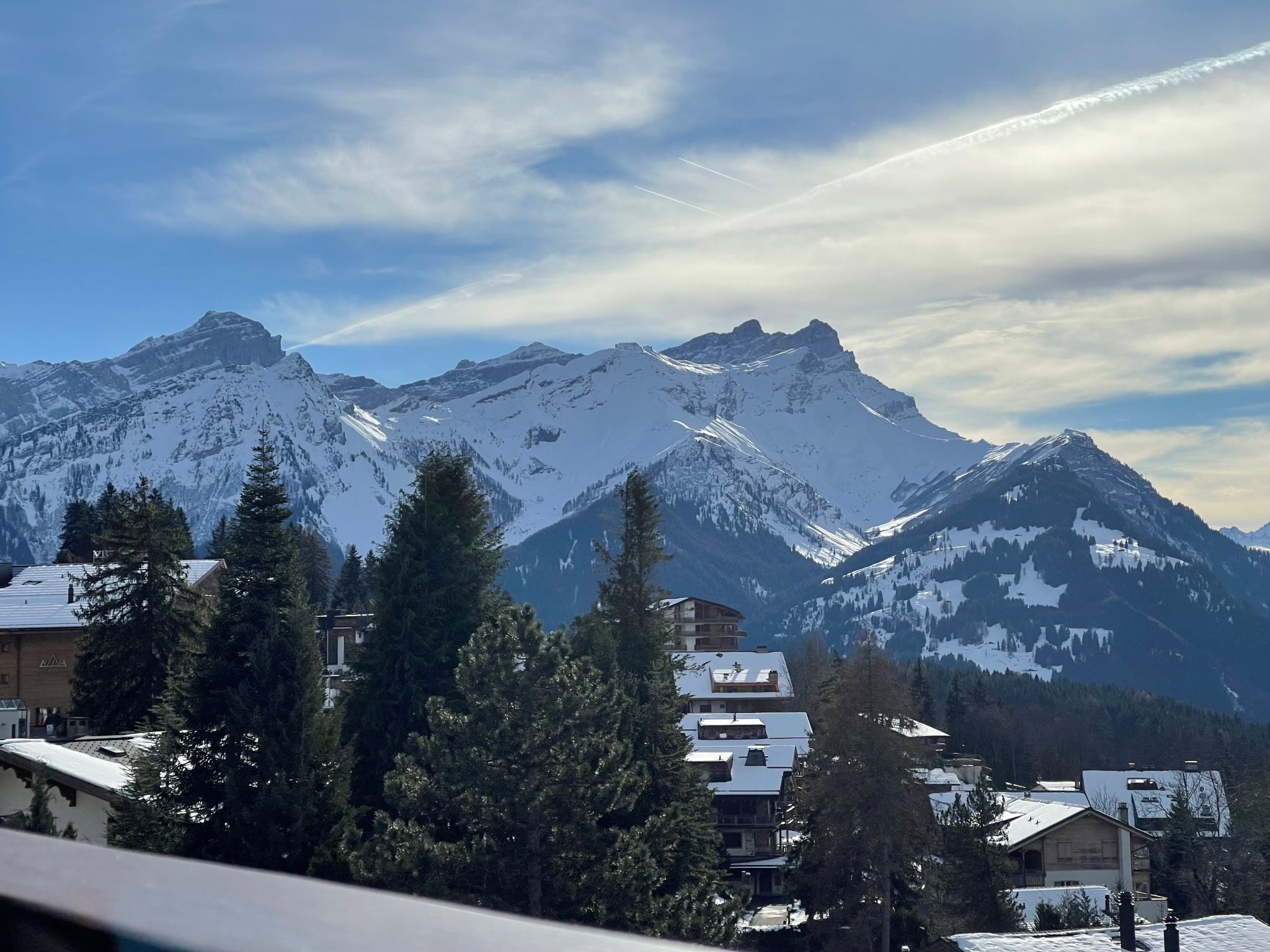 A mountain resort with snow-covered peaks, buildings with sloped roofs, and dense evergreen trees.