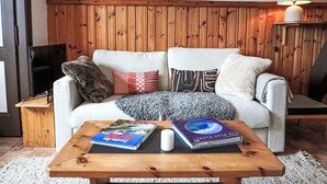 En hyggelig stue med en træpanelfod, en hvid sofa med mønstrede puder, et sofabord med bøger og en lampe på et lille bord.