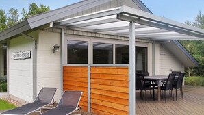 Un espace extérieur abrité, doté d’une terrasse en bois, de deux chaises longues et d’une table avec des chaises.