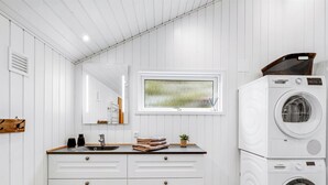 Une salle de bain moderne avec un meuble-lavabo blanc, un grand miroir, une fenêtre et un lave-linge et un sèche-linge superposés.