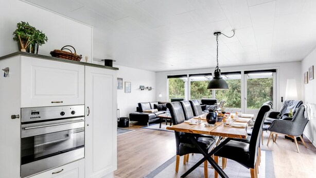 Une cuisine moderne avec des meubles blancs, un four encastré et un coin repas comprenant une table en bois et des chaises noires.