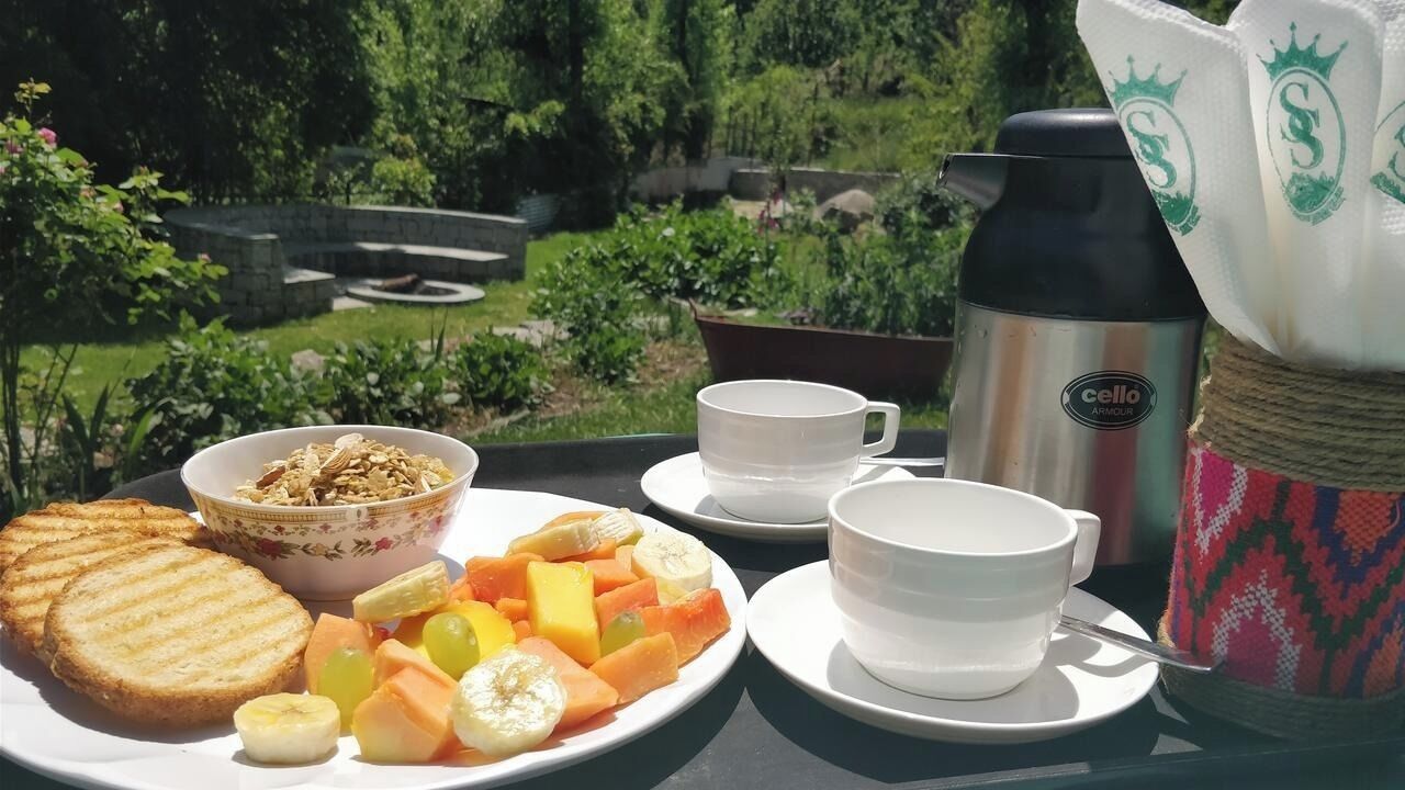 A breakfast setup with toast, cereal, fruit, and coffee on a table with a scenic garden view.