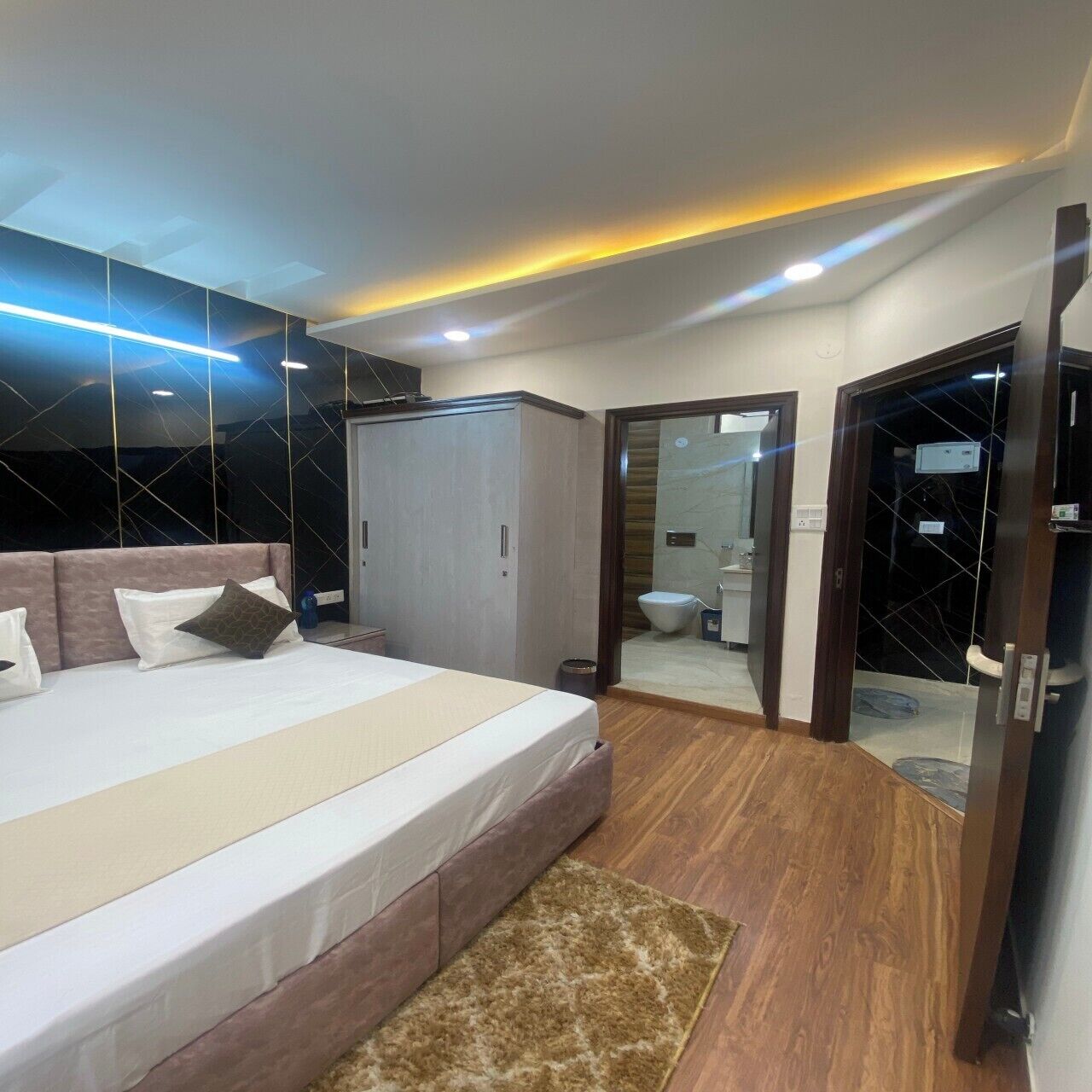 A modern bedroom with a large bed, a wardrobe, and a bathroom visible through an open door.
