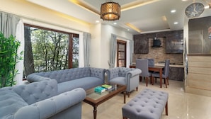 A modern living room with a sectional sofa, a coffee table, and a dining area with chairs and a table. - The Pine Retreat - Mall Road Dalhousie (Dalhousie)