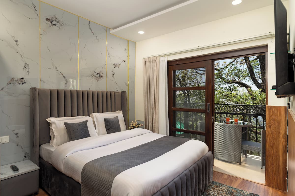 A modern bedroom with a large bed, a nightstand, a TV, and a balcony with outdoor furniture.