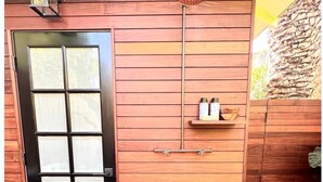 Puerta de madera con paneles de vidrio esmerilado, cabezal de ducha y repisa con artículos de aseo.