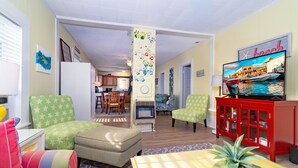A living room with green and white patterned chairs, a red cabinet, and a television displaying a beach scene. - 3 Bdrm in Historic Downtown (Morehead City)
