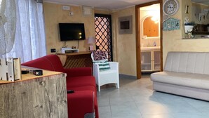 Una sala de estar con un sofá rojo, un sofá blanco, un televisor, una mesita con una lámpara y una ventana con diseño de celosía.
