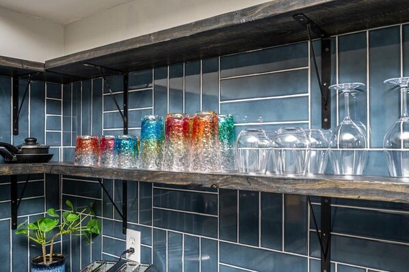 Una cucina con una parete di fondo piastrellata, uno scaffale con barattoli di vetro colorati e una pianta in vaso.