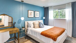 Ein Schlafzimmer mit einem Bett, einem Schreibtisch, einem Spiegel und zwei gerahmten Bildern an der Wand.