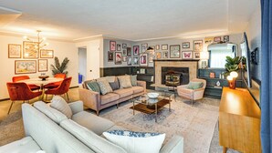 Ein Wohnzimmer mit einer Couch, Sesseln, einem Couchtisch, einem Kamin und gerahmten Bildern an den Wänden.