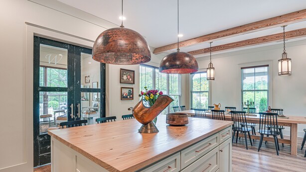 Une cuisine spacieuse dotée d’un grand îlot central, de plans de travail en bois et de luminaires suspendus en cuivre.