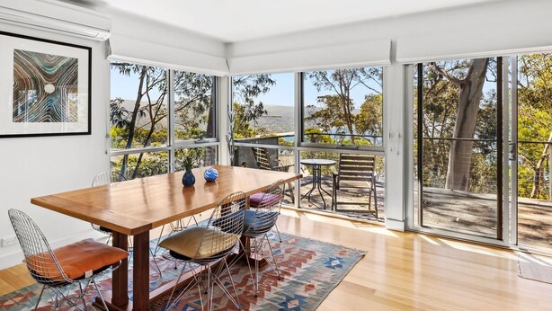 A modern dining area with a wooden table, metal chairs, and a view of the outdoors through large windows.