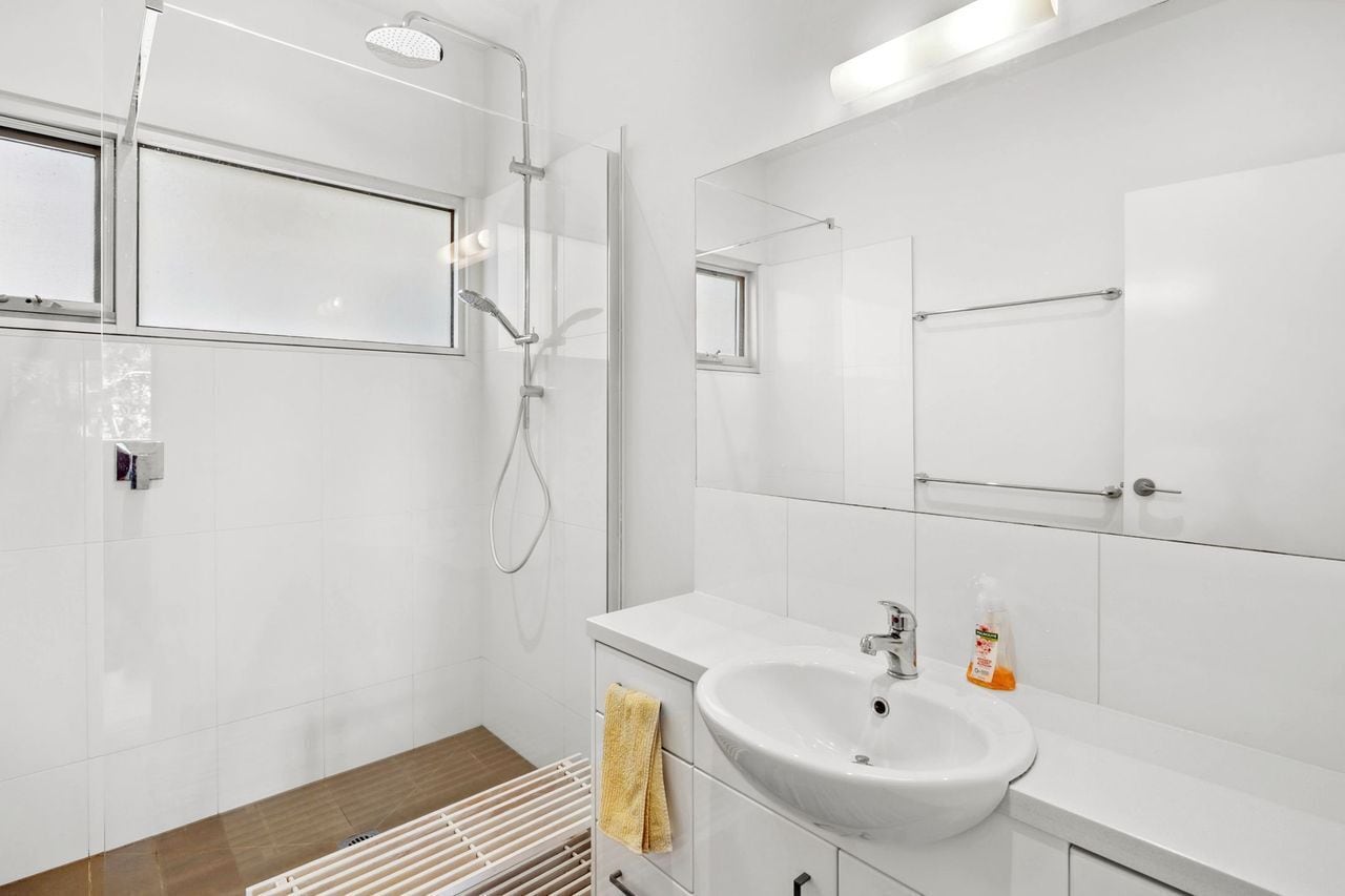 A modern bathroom with a glass shower enclosure, a white sink, and a large mirror.