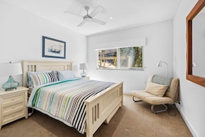 Quarto com cama, mesas de cabeceira, uma cadeira, janela e ventilador de teto.