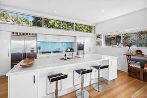 A modern kitchen with a large island, stainless steel appliances, and a view of greenery through the windows.