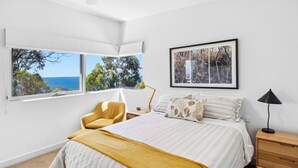 A bedroom with a bed, a chair, a bedside table, a lamp, and a framed picture on the wall.