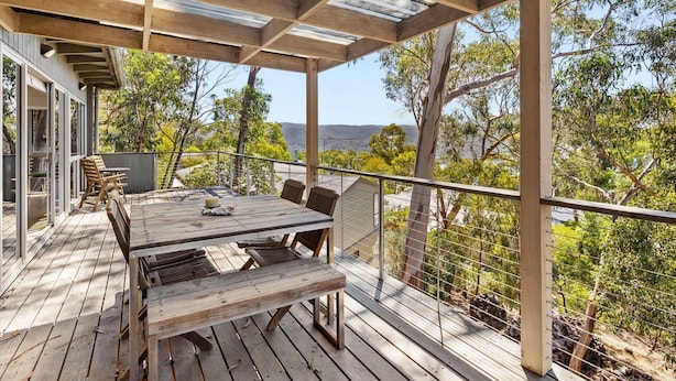 A wooden deck with a table and chairs, overlooking a natural landscape.