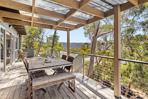 Um deck de madeira com mesa e cadeiras, com vista para uma paisagem natural.