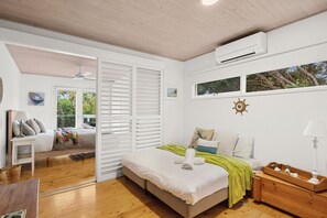 A bedroom with a bed, a wooden dresser, a nightstand, a ceiling fan, and a window with a view of trees.