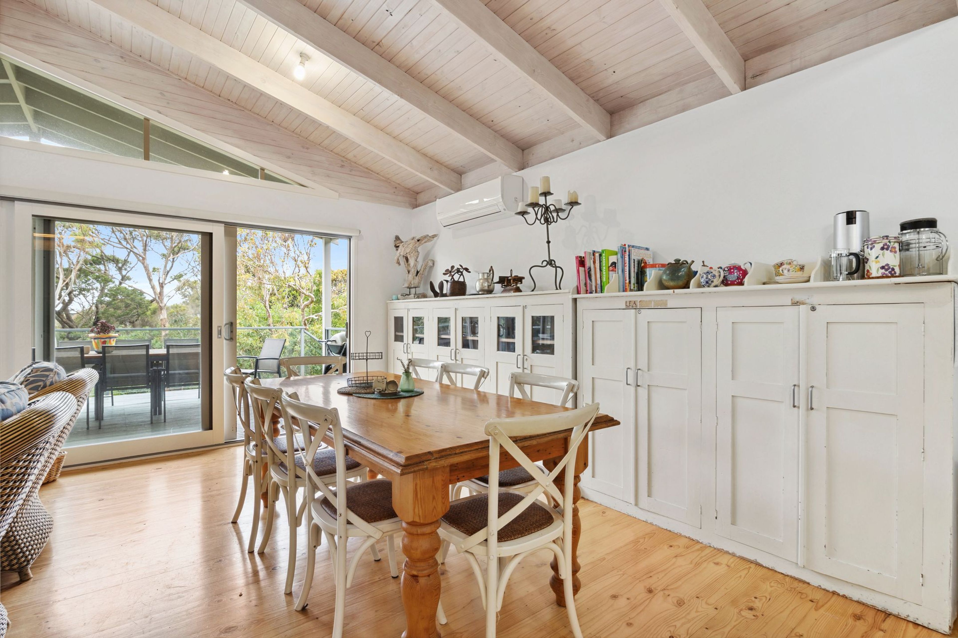 A modern kitchen with a wooden table and chairs, white cabinets, and a view through the glass door to an outdoor deck.