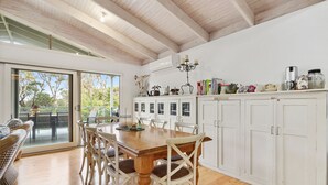 Una cocina moderna con una mesa y sillas de madera, armarios blancos y vistas al exterior a través de una puerta de cristal.