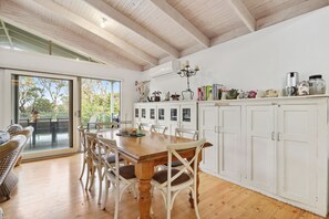 A modern kitchen with a wooden table and chairs, white cabinets, and a view through the glass door to an outdoor deck. - Coastwalk (Aireys Inlet)