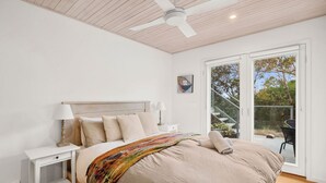 Un dormitorio con cama, mesitas de noche, ventilador de techo y vista a una terraza exterior.