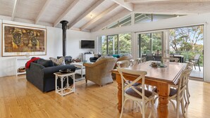 A spacious living area with a high ceiling, a fireplace, a television, and a dining area with a view of the outdoors. - Coastwalk (Aireys Inlet)