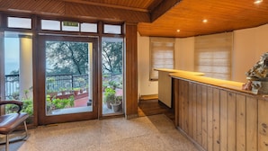Zona de recepción con techo de madera, mostrador de recepción y puerta de cristal que da a un balcón exterior con plantas en macetas.