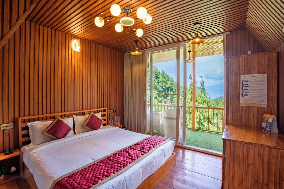A wooden-paneled bedroom with a large bed, a wooden desk, and a balcony with a view of greenery and mountains.