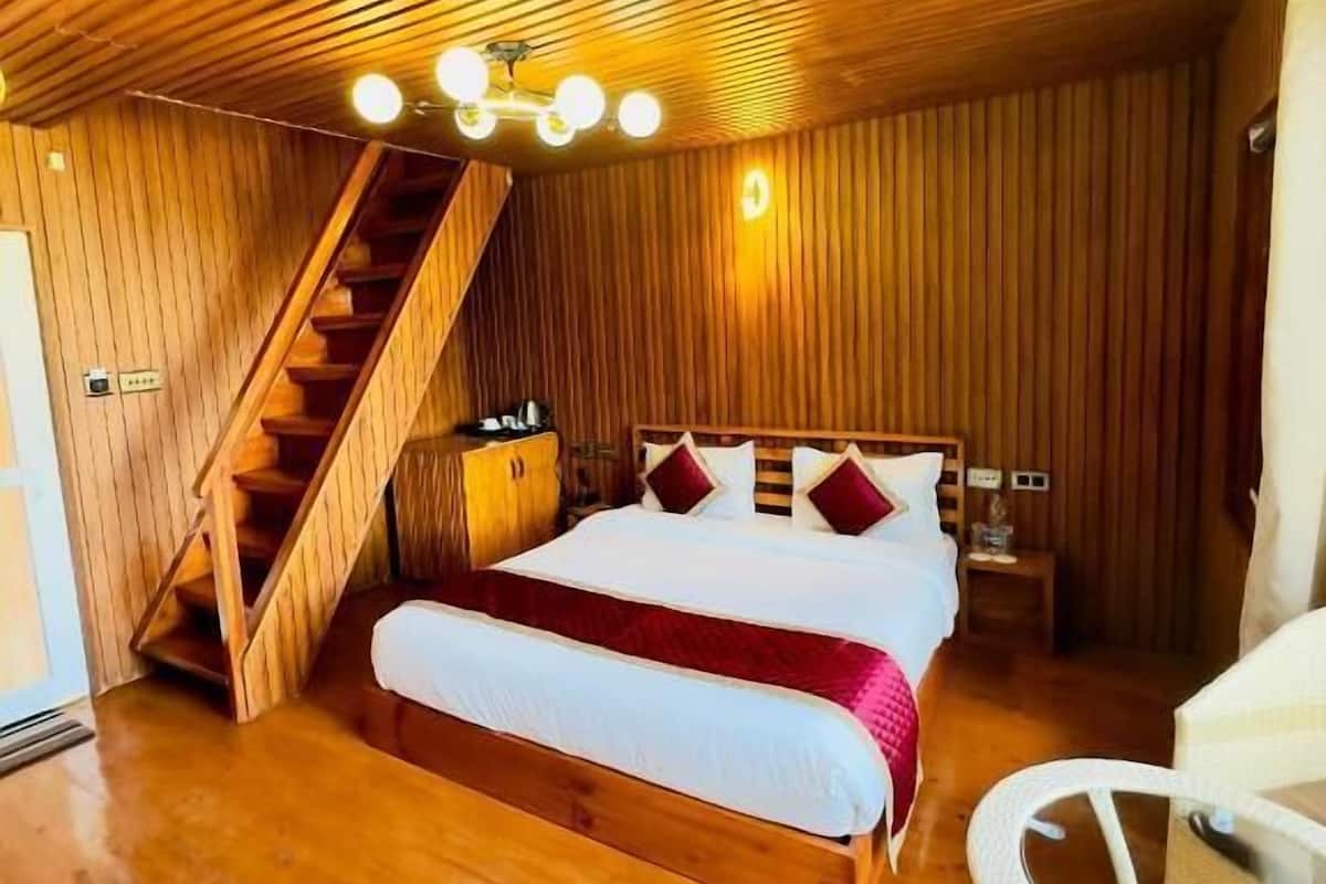 A wooden room with a bed, a chair, a staircase, and a ceiling light fixture.