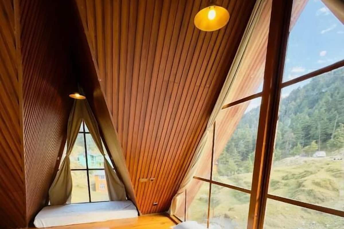 A bedroom with a large bed, wooden walls, and a view of a forested landscape through a window.