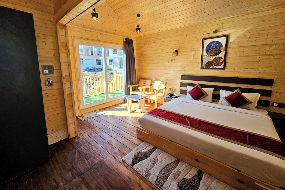 A wooden cabin room with a bed, a desk, and a chair.