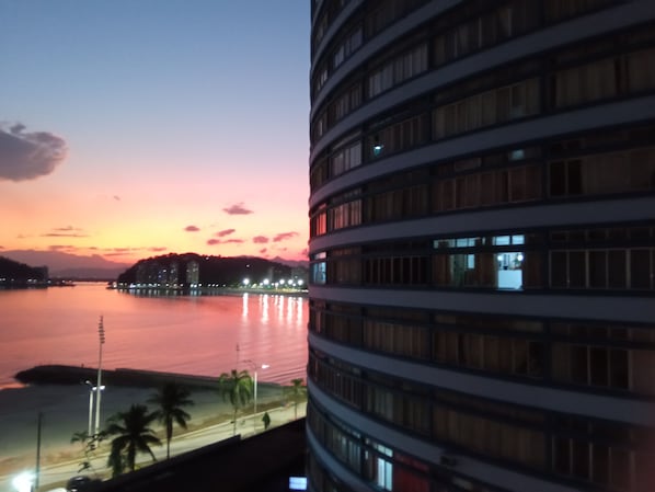 A high-rise building with multiple floors, large windows, and a view of a sunset over a body of water.