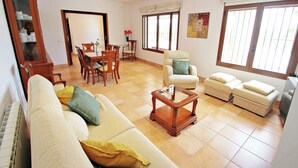 A living room with a sofa, armchairs, a coffee table, and a dining area with chairs and a table.