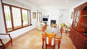 A spacious dining area with a long wooden table and chairs, a sofa, and a TV in the background.