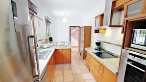 A modern kitchen with stainless steel appliances, wooden cabinets, and a tiled floor.